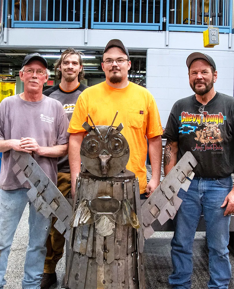Team posing with metal sculpture of an owl at Metal Mania