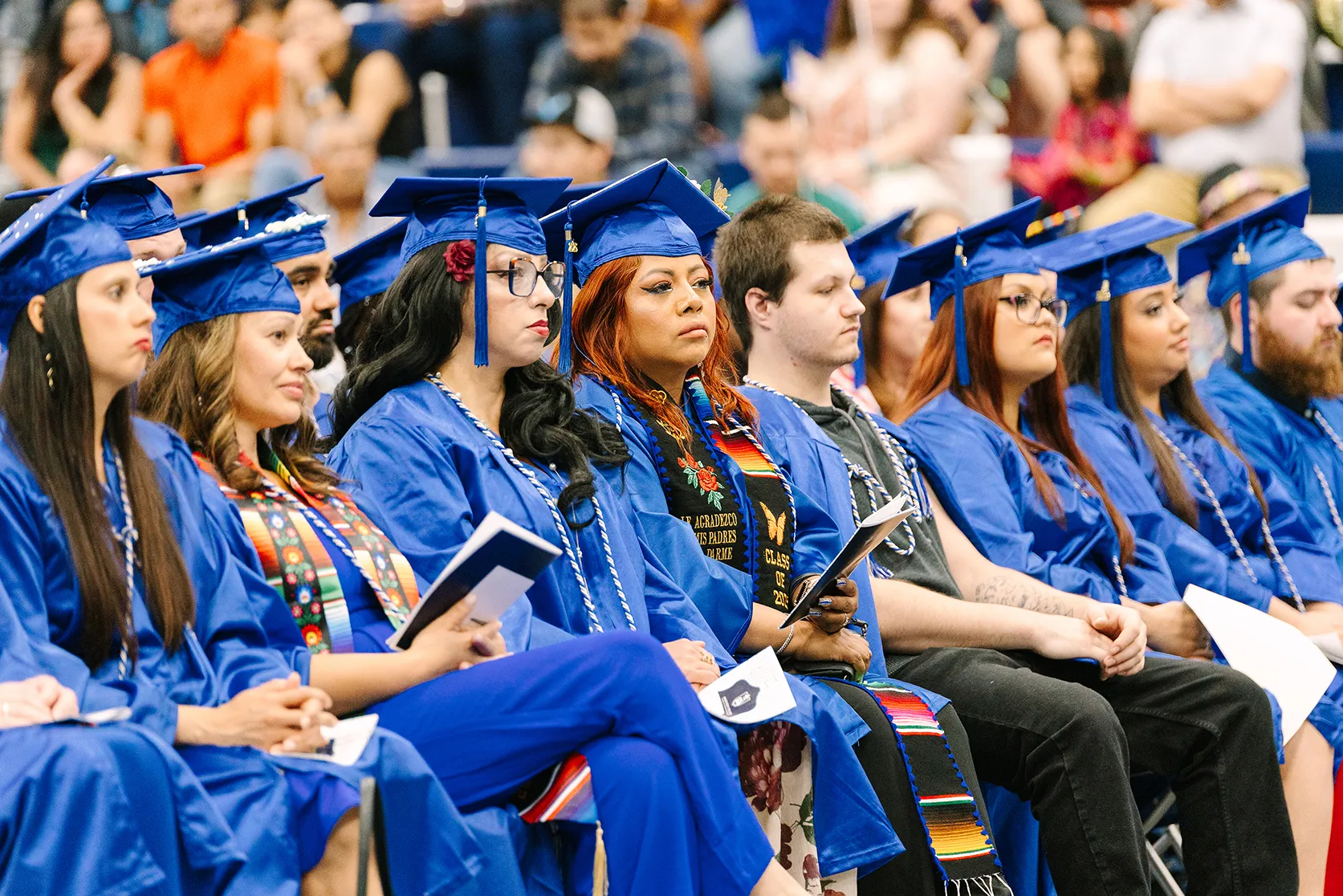Graduate of the 2025 High School Equivalency Program sitting during ceremony wearing blue caps and gown.