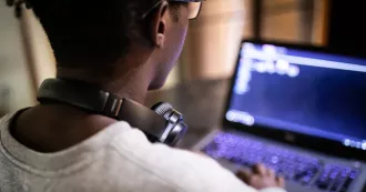 Man uses laptop computer with headphones around his neck. 