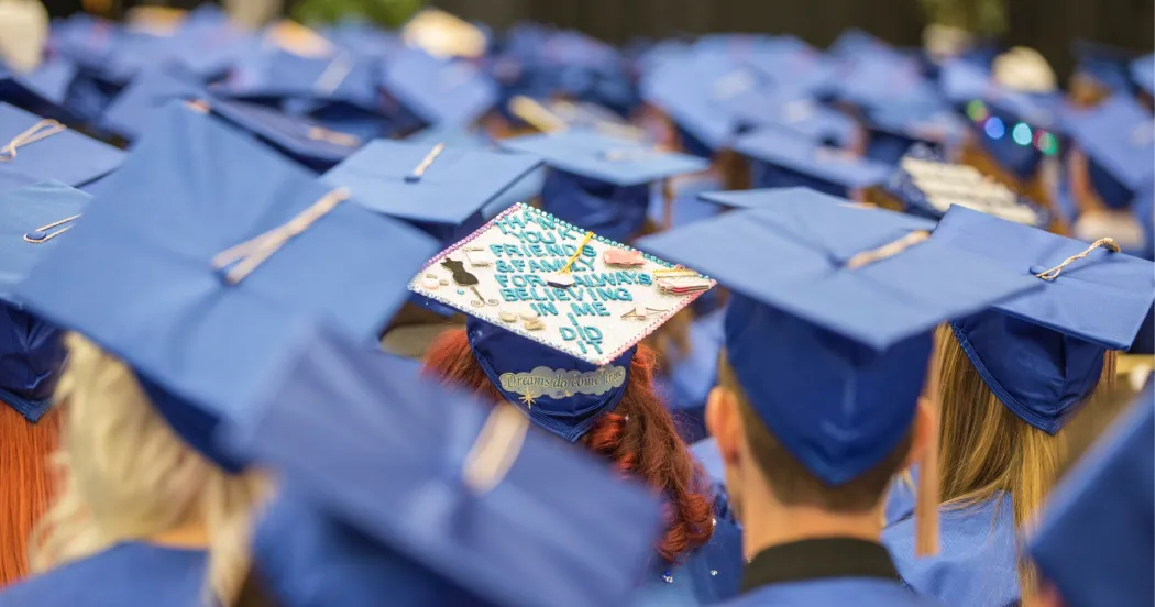 Photo of students at graduation ceremony, viewed from the back, showing their caps.