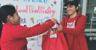 Peer Health Educators Michel and Riley distribute red food pantry bags in the front of the Health Education Building at the Truax campus.
