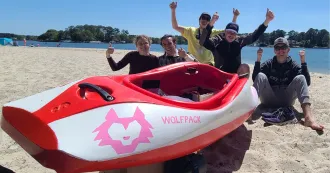 Photo of Madison College students posing on a sand beach with their competition boat.