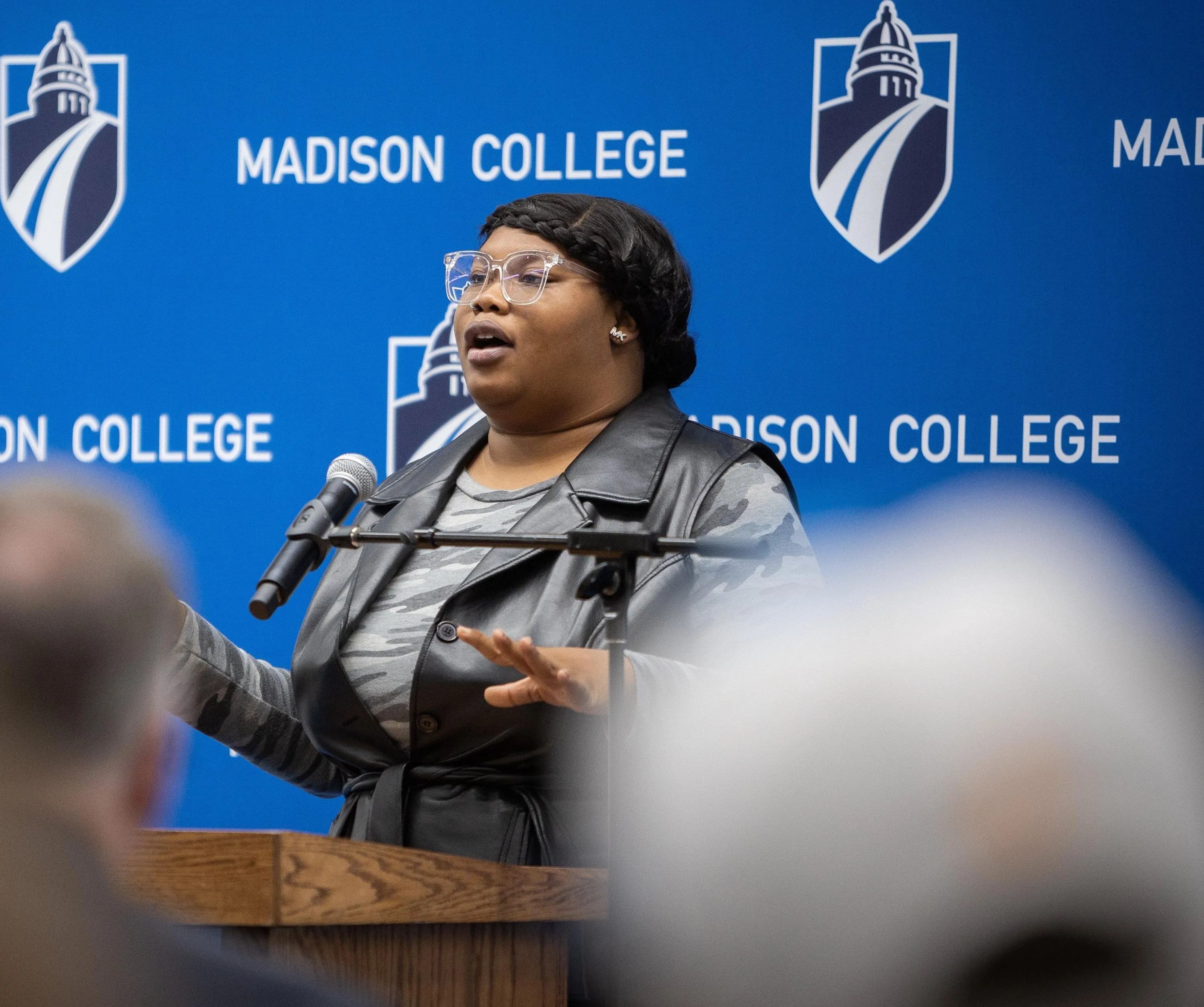 Madison College student Dacara Cooper speaks at the Madison College Goodman South Early Learning Campus celebration with a blue Madison College logo banner behind her.