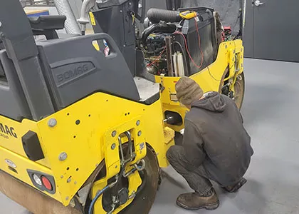 person bending down repairing heavy equipment