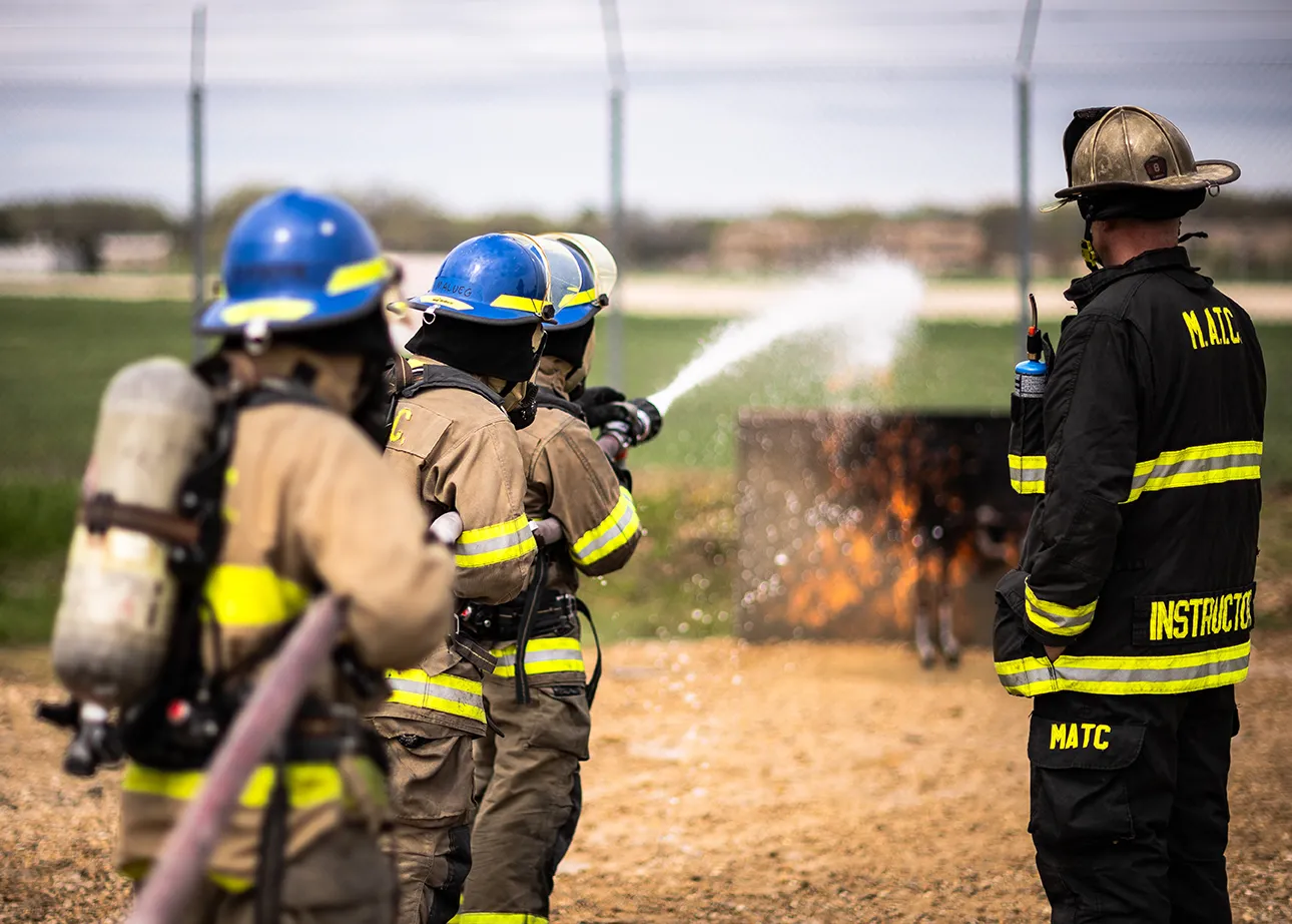 three students and an instructor in fire fighter gear putting out a test fire. 
