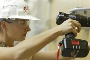Student in hard hat using a cordless drill to mount an unseen item on wall