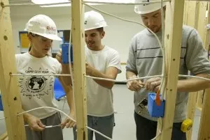 Three students roughing in insulated electrical wires aka romex in wood frame construction