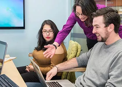 A teacher showing two students something on a laptop
