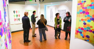 People in the middle of a gallery exhibit talking and looking at art work on the walls.