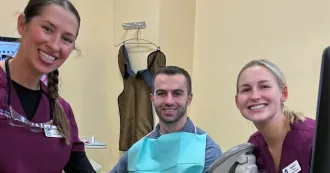Two dental hygienist pose with a person receiving dental care.