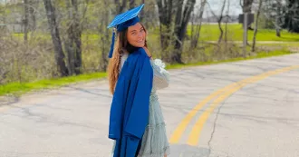 Heather wears her graduation cap and holds gown over shoulder. 