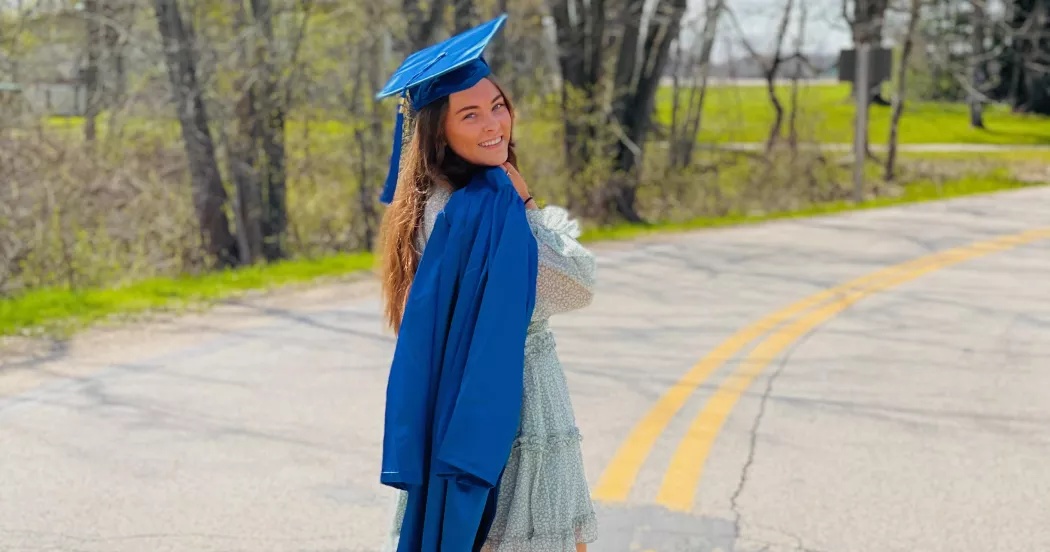 Heather wears her graduation cap and holds gown over shoulder. 