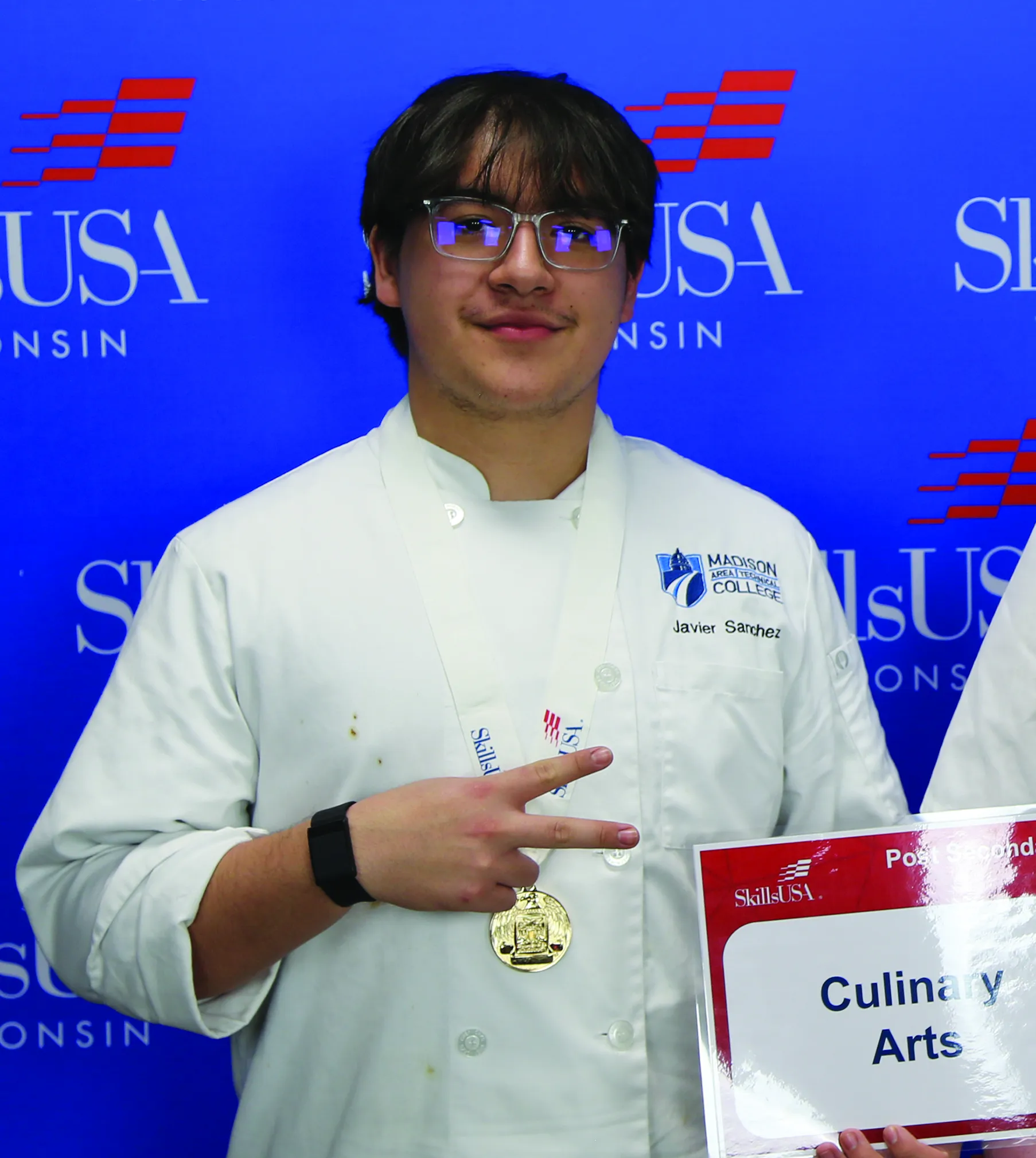 2025 SkillsUSA gold medalist Javier Sanchez poses with his gold medal with a blue SkilsUSA logo behind.