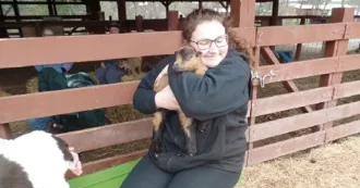 Kailyn Ripp kneeling and snuggling a baby farm animal in front of corral