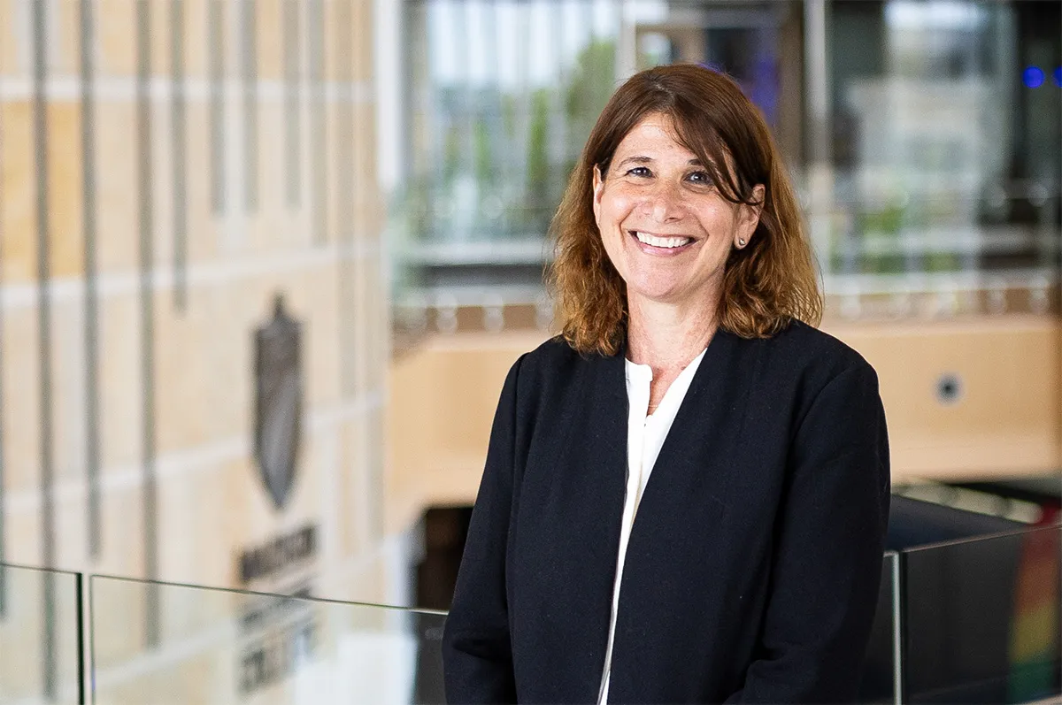 Dr. Jennifer Berne standing next to Madison College shield logo wall