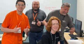 Photo of Mini Manufacturing World participants in classroom around computer.