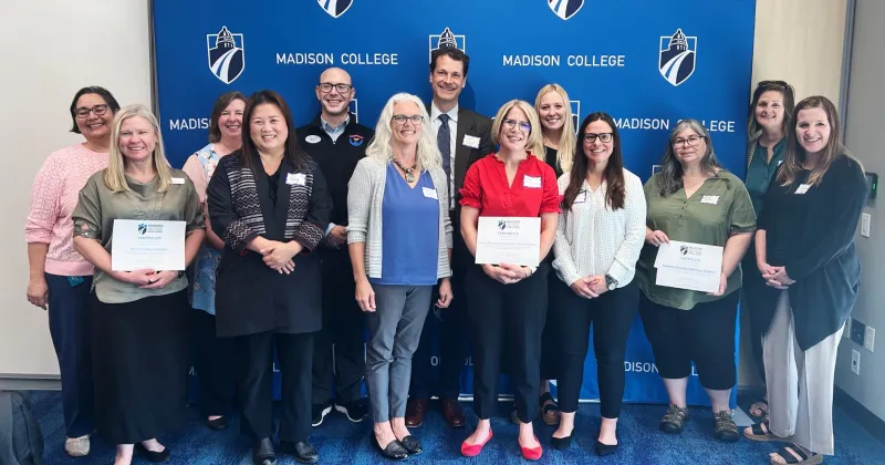 Madison College employees and community partners posing for a photo in front of a blue Madison College banner backdrop.