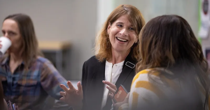 President Jennifer Berne, wearing dark blazer, talking with a person in a yellow striped sweater.