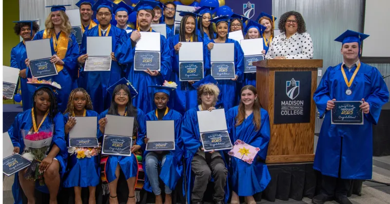 A group of Gateway College posing with their diplomas/certificates, dressed in blue caps and gowns.