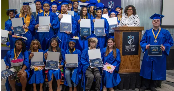 A group of Gateway College posing with their diplomas/certificates, dressed in blue caps and gowns.
