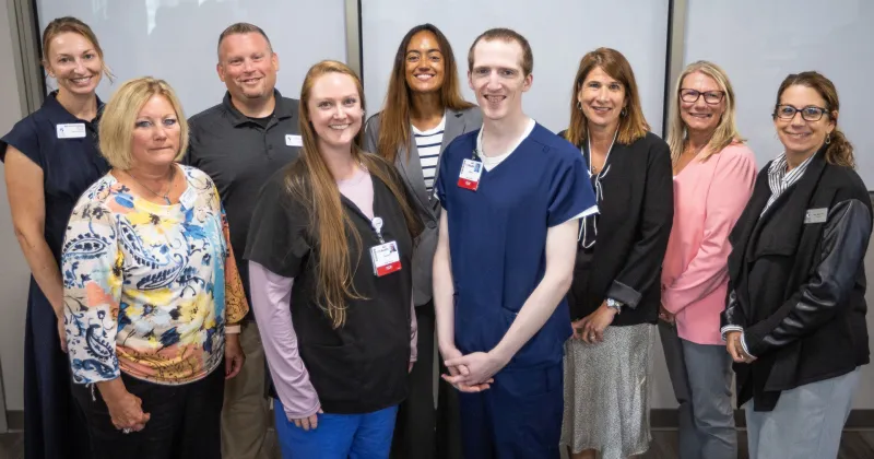 Two surgical technology apprenticeship pose, wearing scrubs, pose for a photo with Madison College President Jennifer Berne and other staff and faculty.