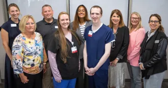 Two surgical technology apprenticeship pose, wearing scrubs, pose for a photo with Madison College President Jennifer Berne and other staff and faculty.