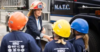 President Berne, wearing a firefighter helmet, shakes hands with young girls in the CampHero program.