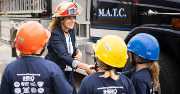 President Berne, wearing a firefighter helmet, shakes hands with young girls in the CampHero program.