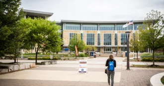 A student walking outside the front of the Madison College Truax campus entrance.