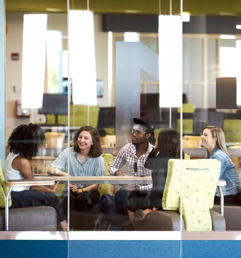 Group of five students working together in a library study room